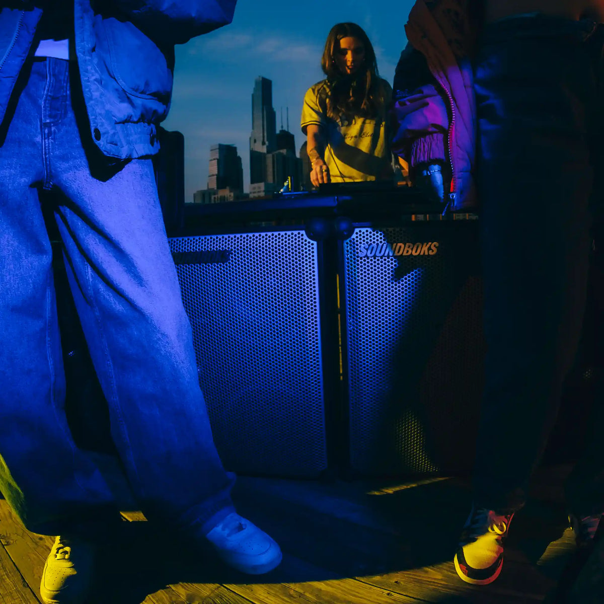 Peoble standing in front of a two Metallic grey Soundboks 4 with a city skyline in the background.